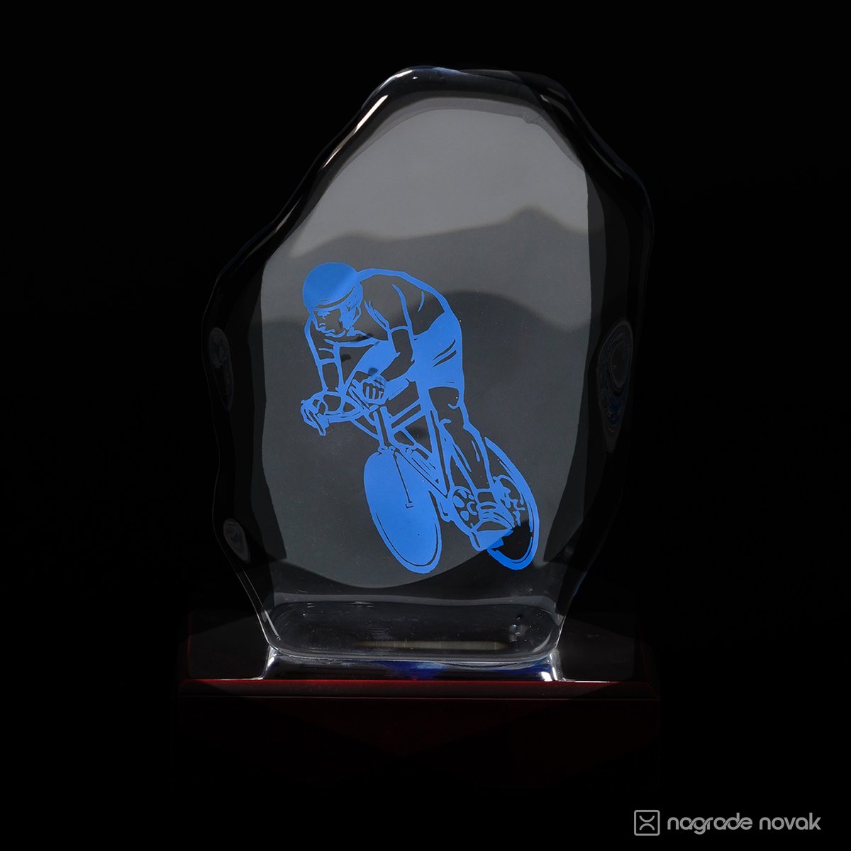 Clear cast glass award with a blue cyclist graphic, seen from the front on a dark wooden base against a black background