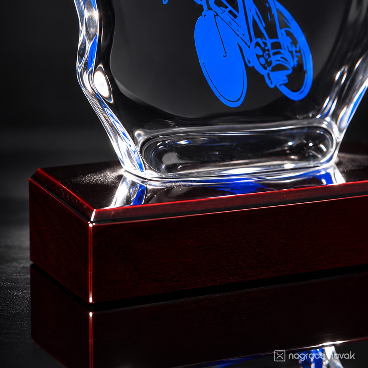 Close-up of the glass base and rear wheel of the blue cyclist motif, resting on a glossy dark red wooden base