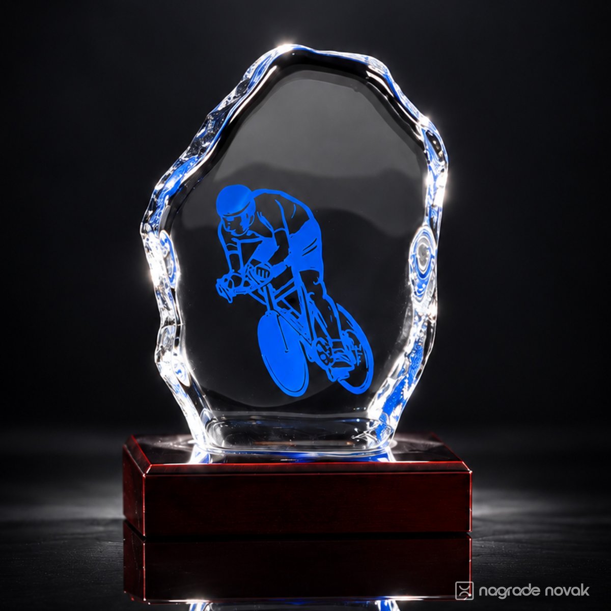 Cast glass award with blue cyclist graphic on a glossy dark red wooden base, lit against a dark background