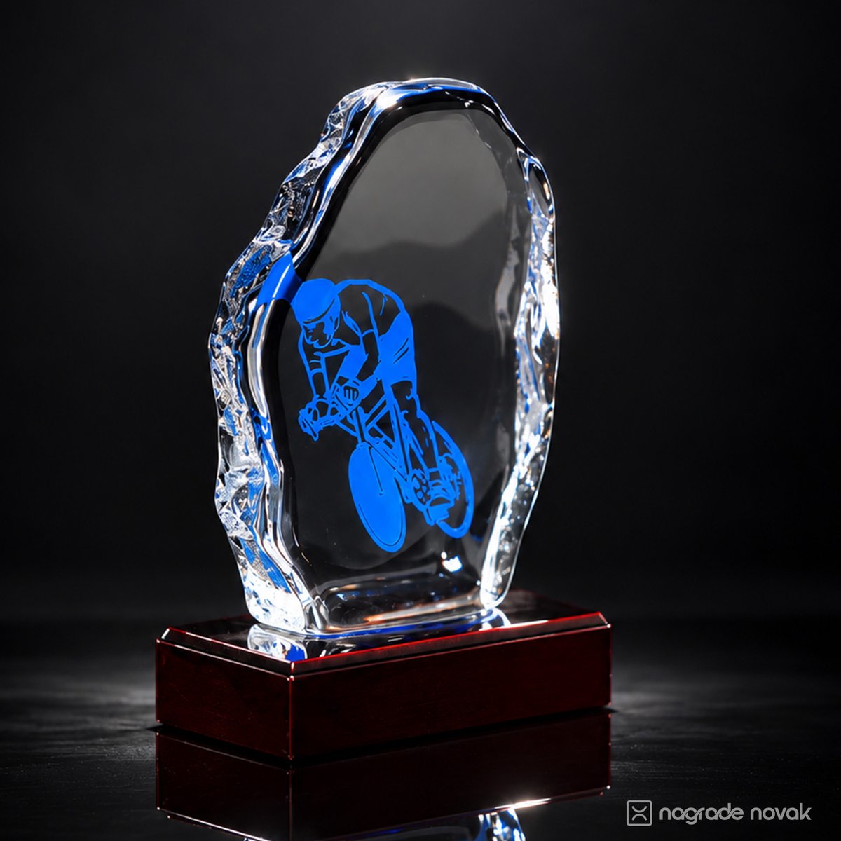 Cast glass award with blue cyclist graphic, seen from a three-quarter angle, with textured glass edge on a dark red wooden base
