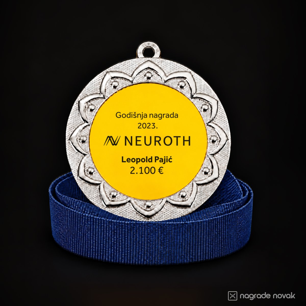 Silver medal with a petal-shaped embossed border and a yellow insert with the Neuroth logo and a personalised name and amount, standing on a coiled dark blue ribbon on a dark background