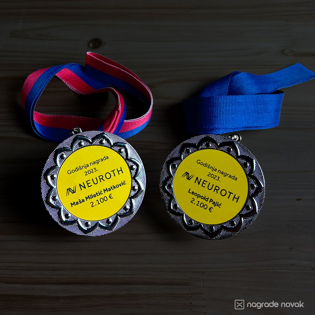 Two silver medals with yellow Neuroth inserts on a dark wooden surface, one with a blue and red ribbon in the Dinamo colours and one with a blue ribbon in the Hajduk colours
