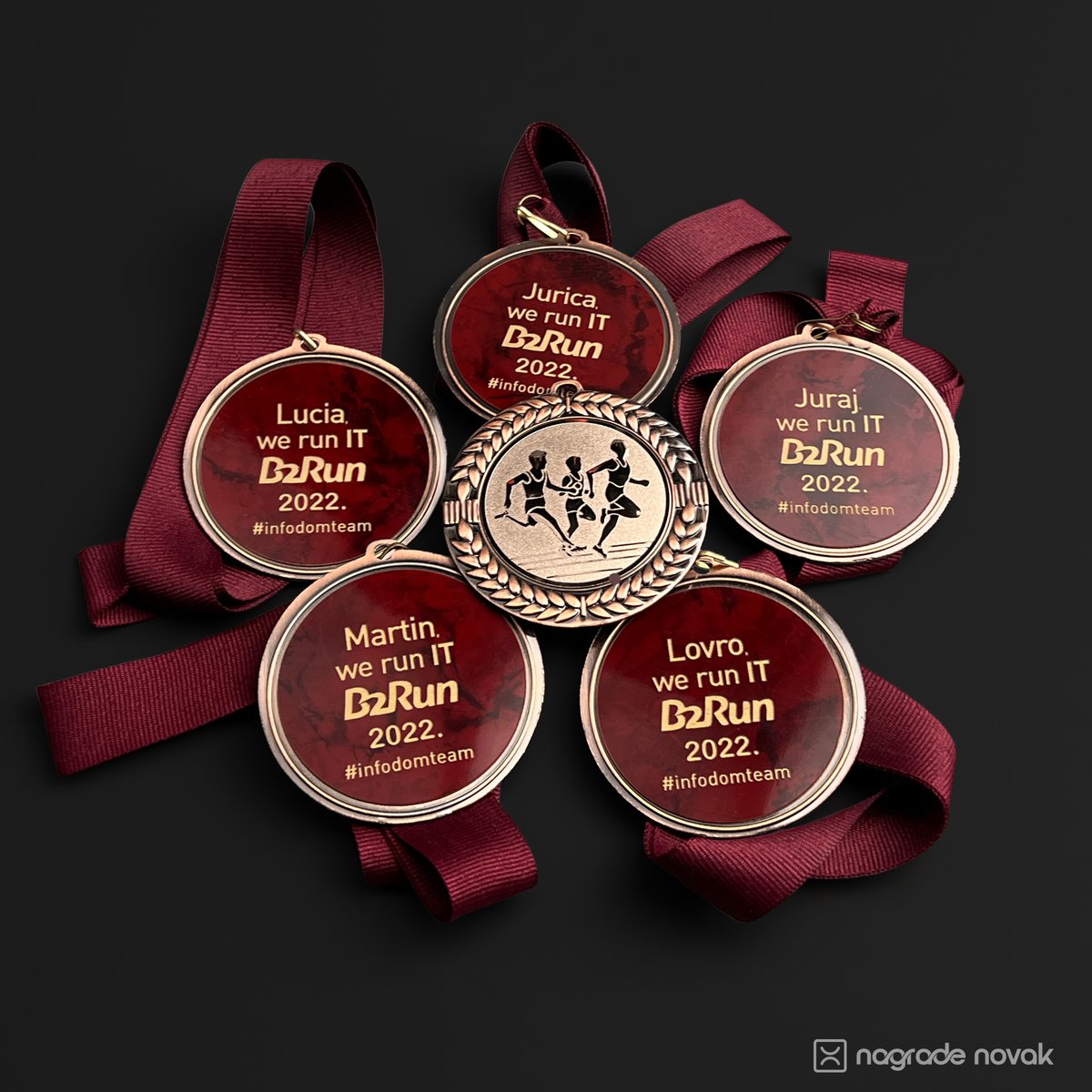 Five maroon medal back inserts personalised with participant names, “we run IT B2Run 2022” and #infodomteam, arranged around the front of a bronze medal with maroon ribbons
