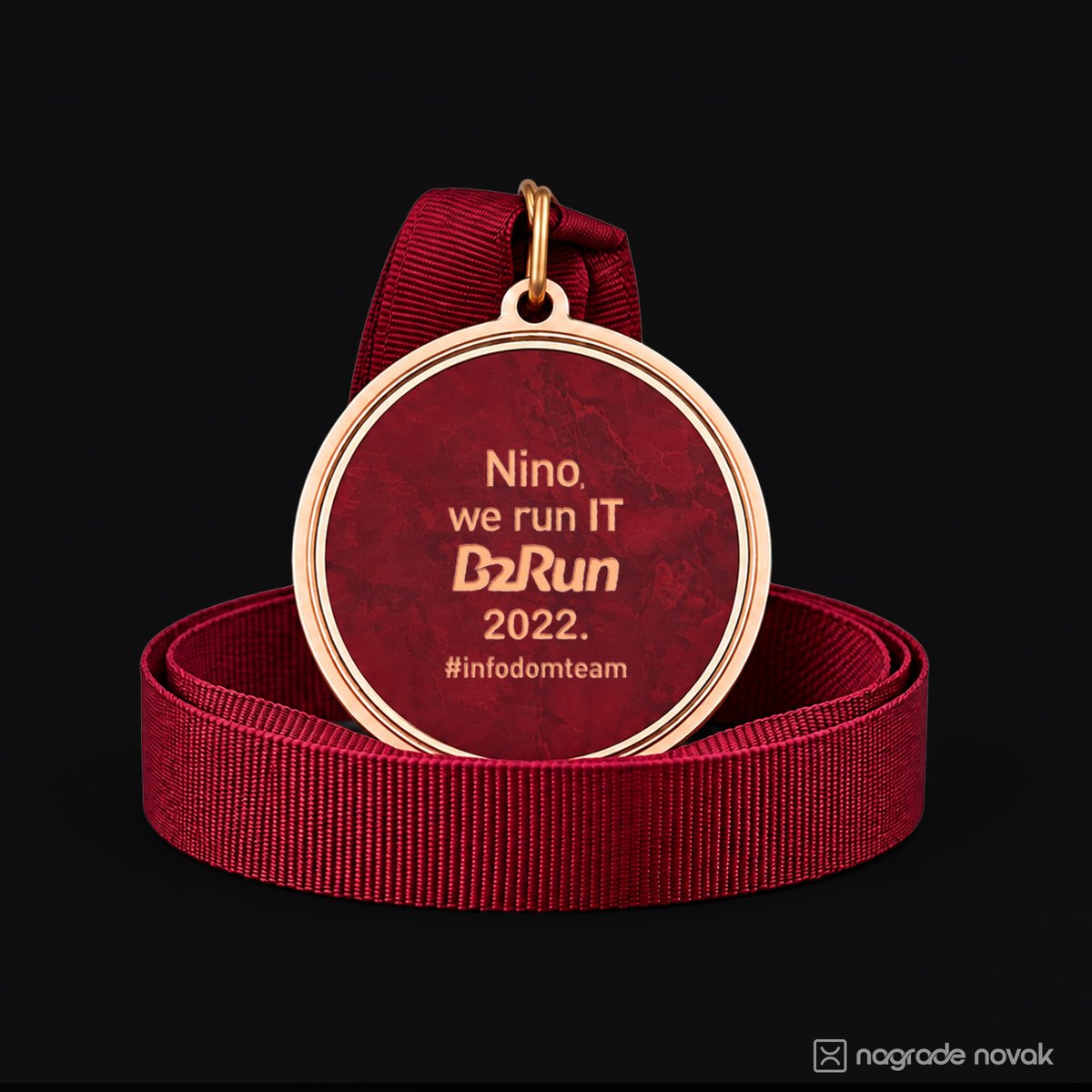 Maroon and gold medal back insert reading “Nino, we run IT B2Run 2022”, resting on a coiled maroon ribbon on a black background