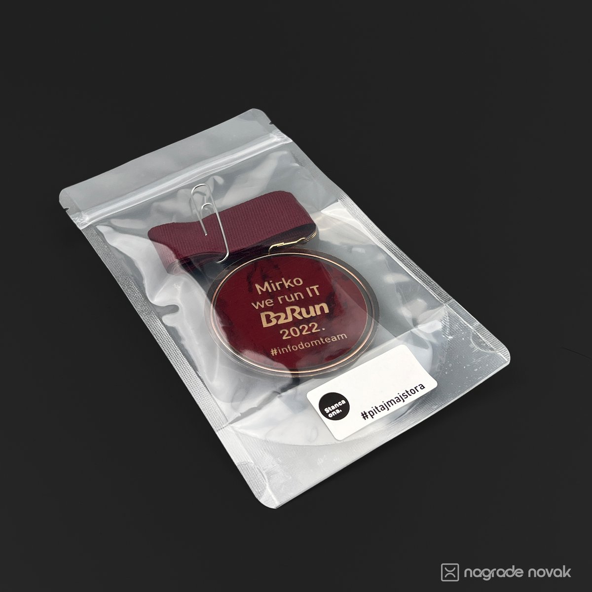 Medal personalised with “Mirko, we run IT B2Run 2022” packed in a clear zip bag, with a paper clip on the maroon ribbon and a white Stancaona label, on a dark background
