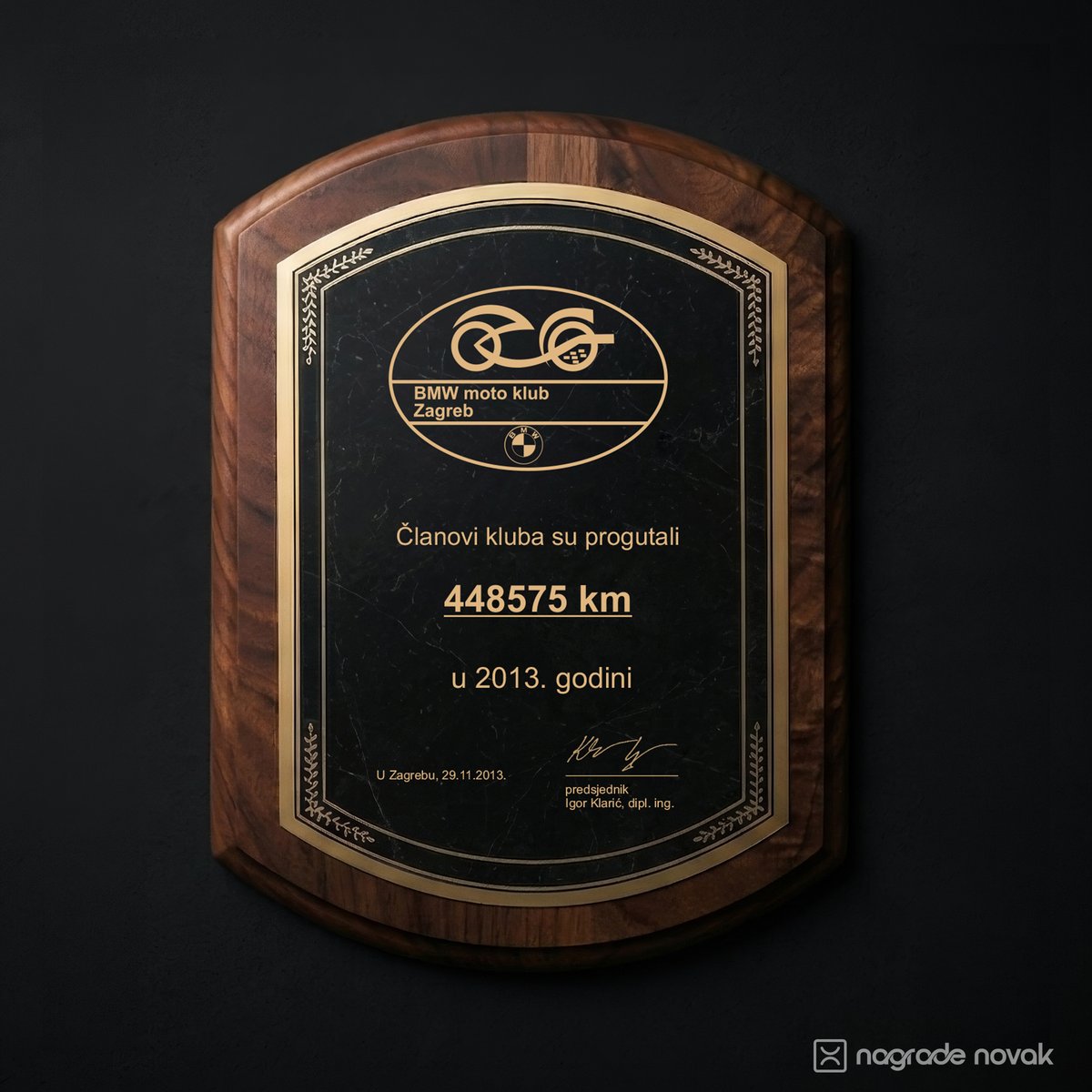 Shield-shaped walnut wooden plaque with a black marbled plate and gold border, engraved with a BMW moto club Zagreb logo and text, on a dark wall