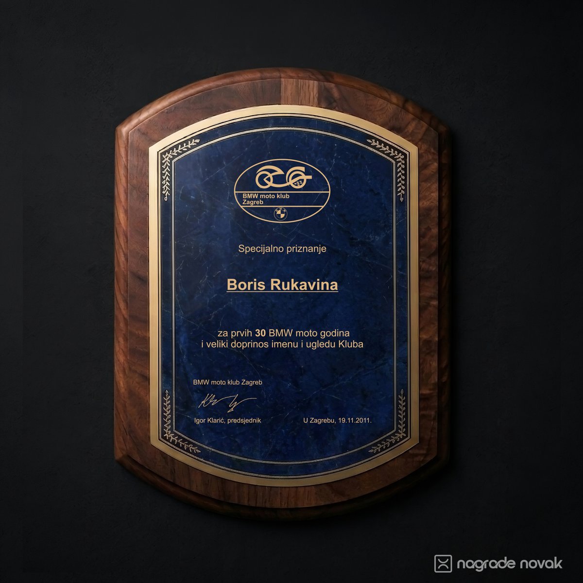 Shield-shaped walnut wooden plaque with a blue marbled plate and gold border, engraved with a special recognition for a club member, on a dark wall