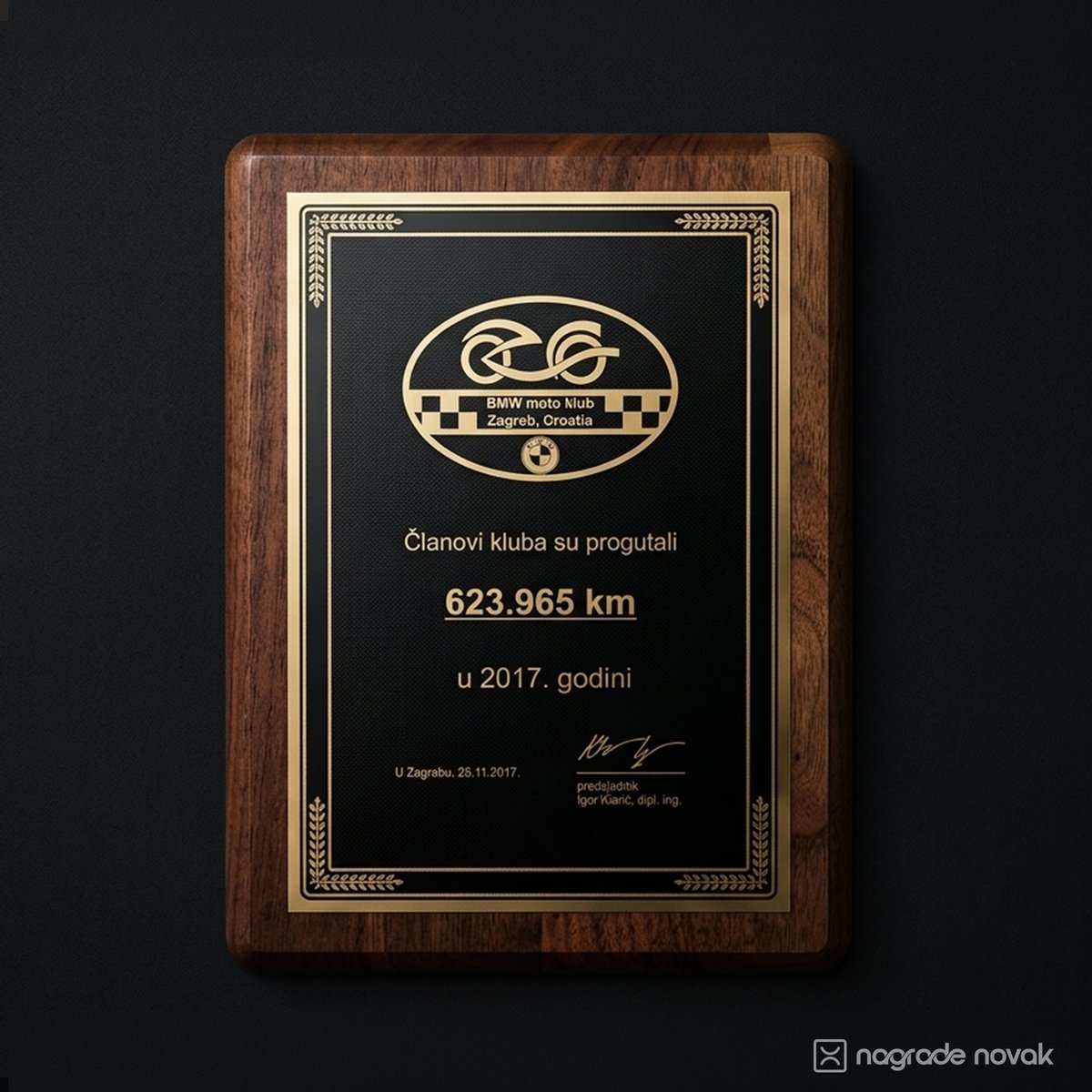 Rectangular walnut wooden plaque with a black plate and gold ornamental border, engraved with a BMW moto club Zagreb, Croatia logo and a kilometre total, on a dark wall
