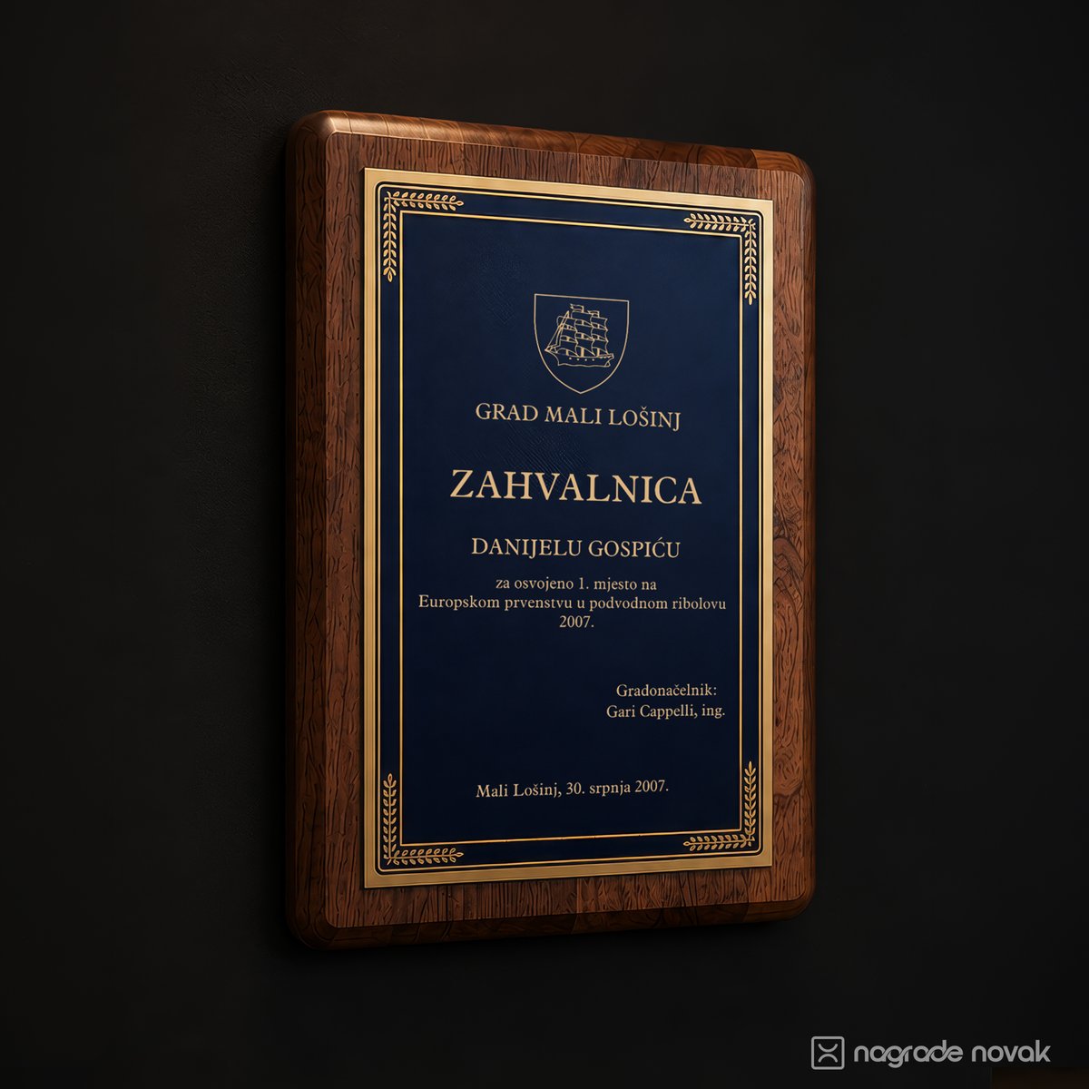 Rectangular walnut wooden plaque with a deep blue plate and gold border, engraved with a certificate of appreciation from the town of Mali Lošinj, on a dark wall