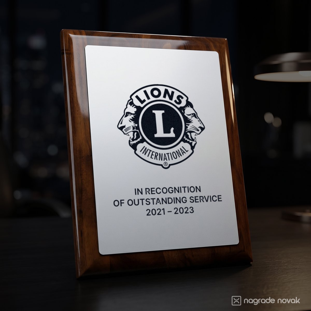 Glossy walnut wooden plaque with a white plate printed with the Lions International logo and the text In recognition of outstanding service 2021–2023, standing on a desk