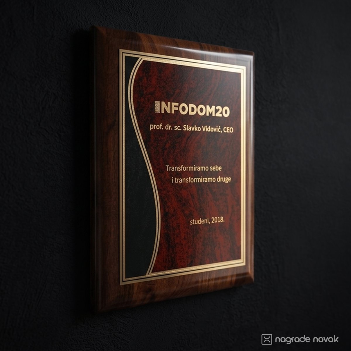 Glossy wooden plaque with a wavy burgundy and black plate and gold engraved Infodom20 logo and text, seen at an angle on a dark wall