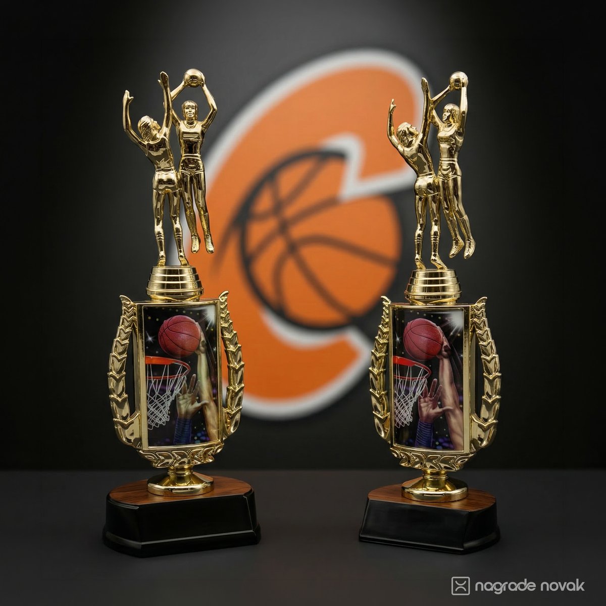 Two gold basketball figurine trophies side by side in front of a blurred orange club logo