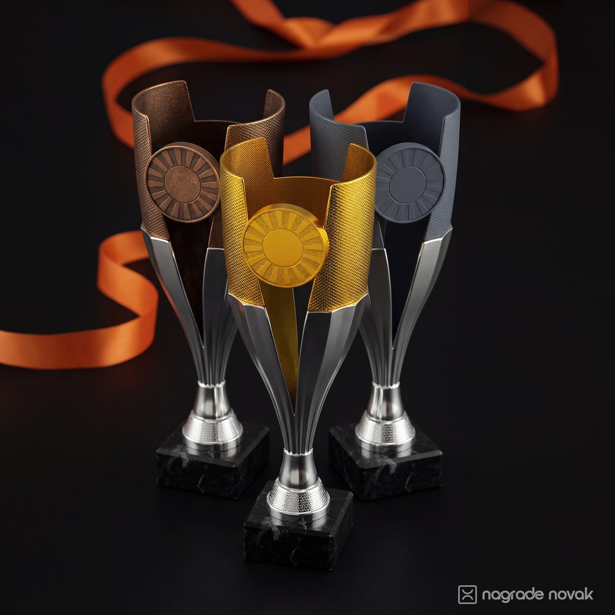 Three tall trophies in bronze, gold and silver on black marble bases, seen from another angle, with an orange ribbon