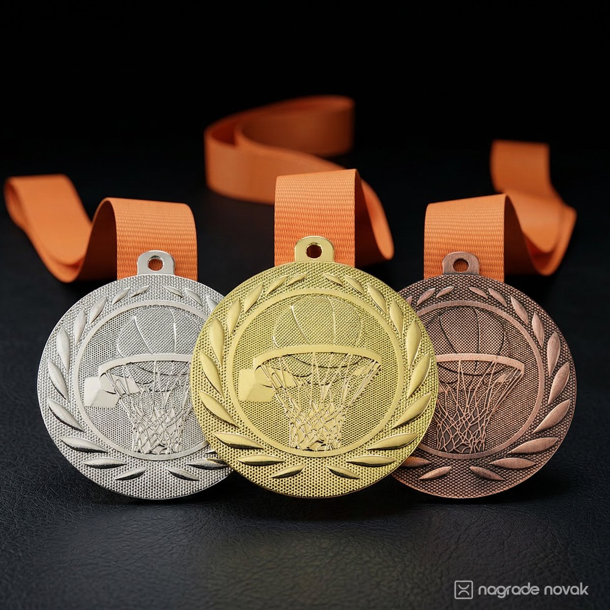 Silver, gold and bronze basketball medals standing upright, with orange ribbons on a dark surface