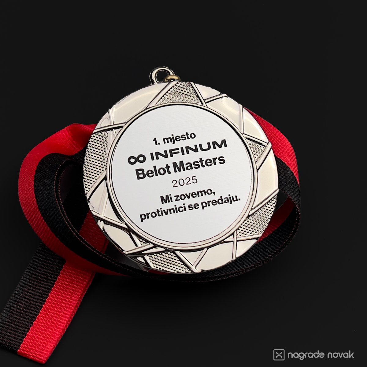 Close-up of the Infinum Belot Masters first-place silver medal with a red and black ribbon, displayed on a dark surface