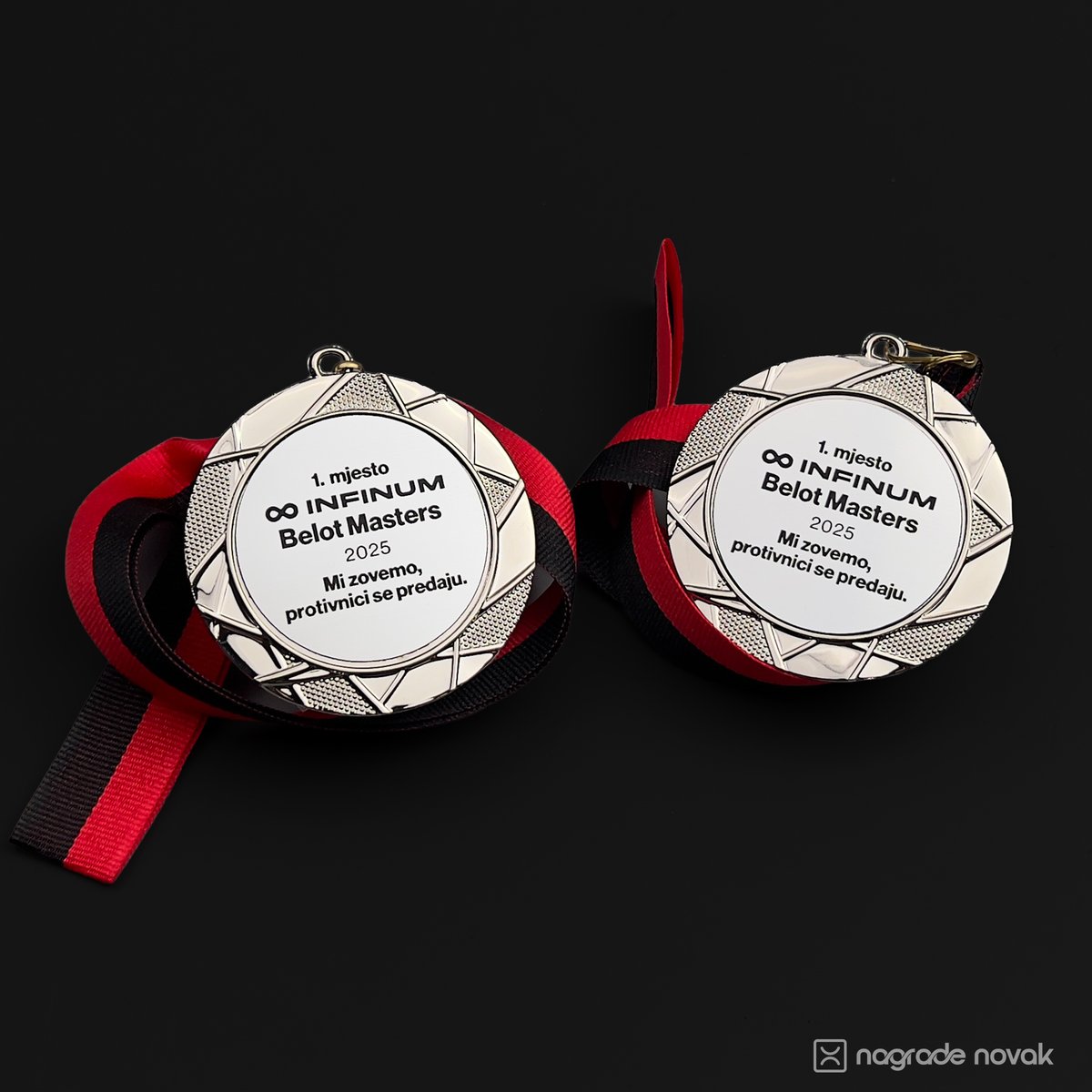 Two round silver medals with red and black ribbons placed side by side on dark fabric.