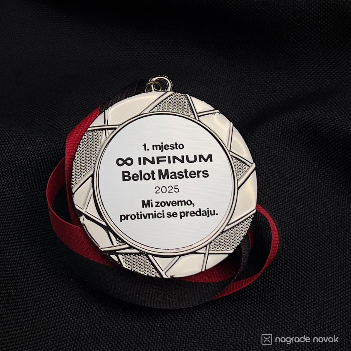 Close-up of a round silver medal with a red and black ribbon, displayed on dark fabric.