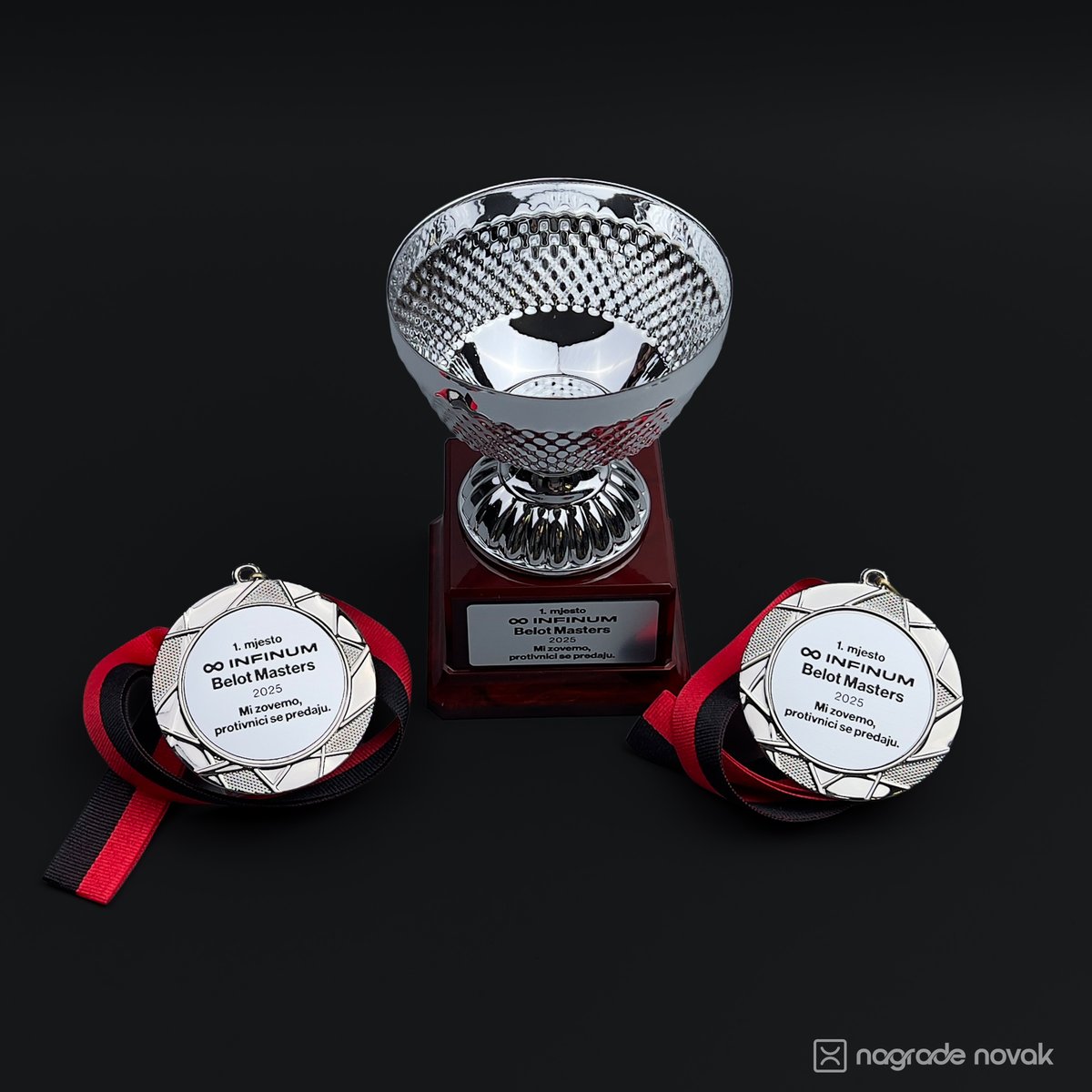 Silver trophy cup on a dark red base positioned next to two round silver medals with ribbons.