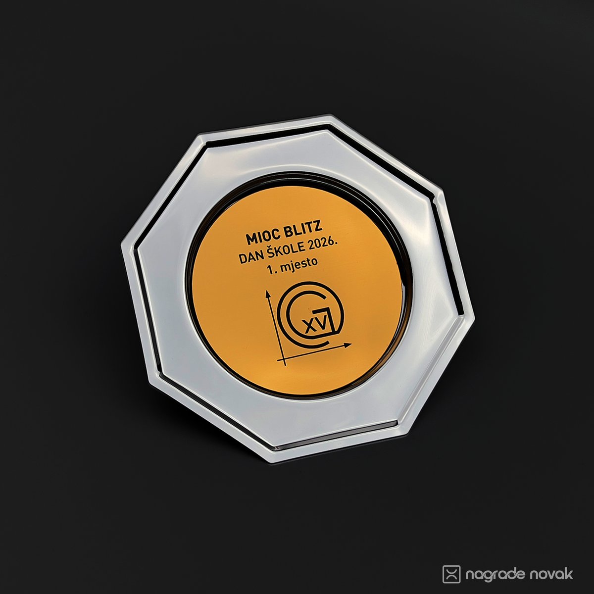 Octagonal silver plate award with a round highly reflective gold insert reading "MIOC BLITZ, DAN ŠKOLE 2026., 1. mjesto" with the school logo, on a dark background