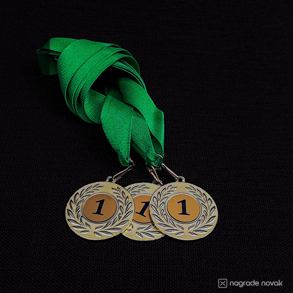 Three medals with a laurel rim and a black number 1 on a gold centre, hanging from a green ribbon on a black background