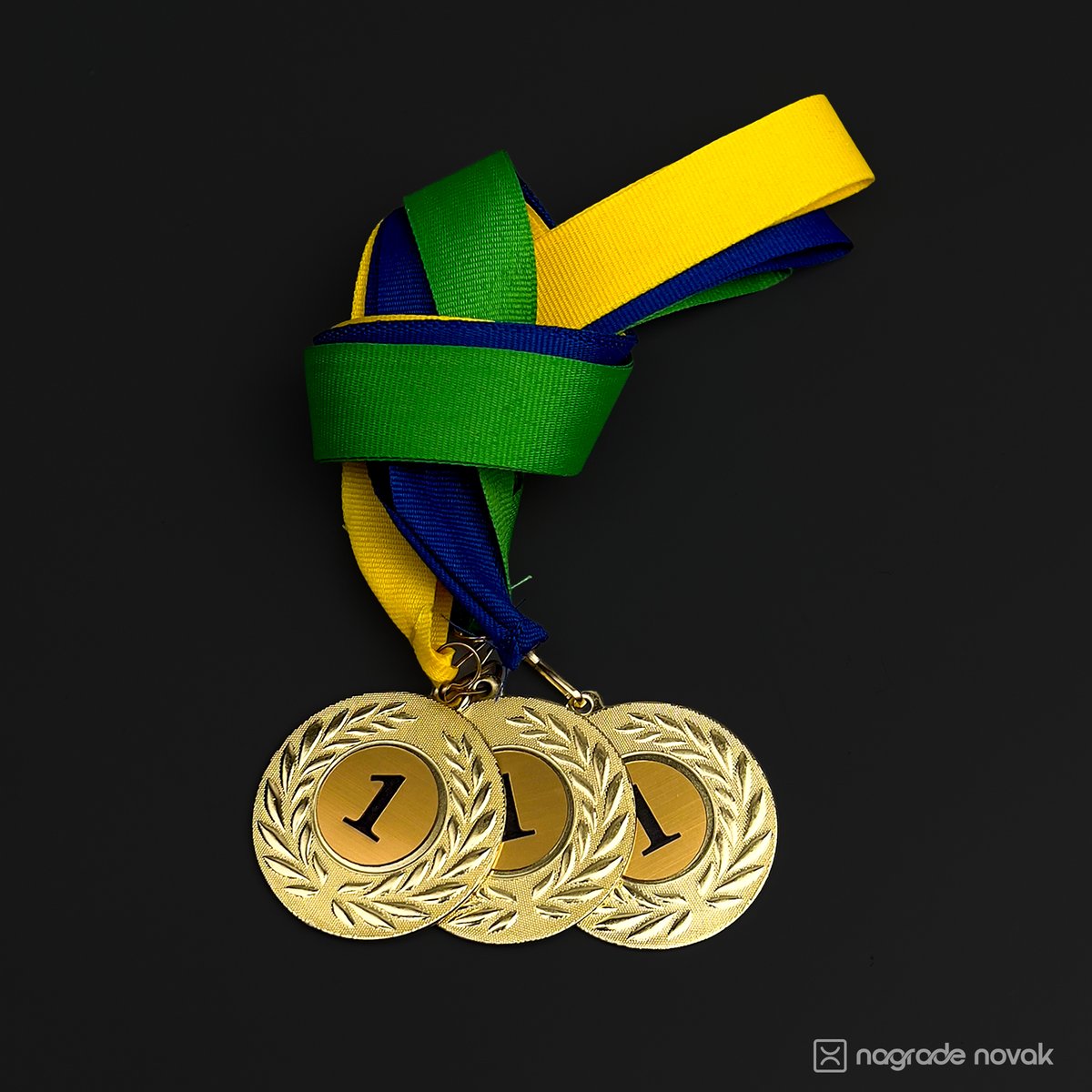 Three gold medals with the number 1 and a green, blue and yellow ribbon, lying on a dark surface