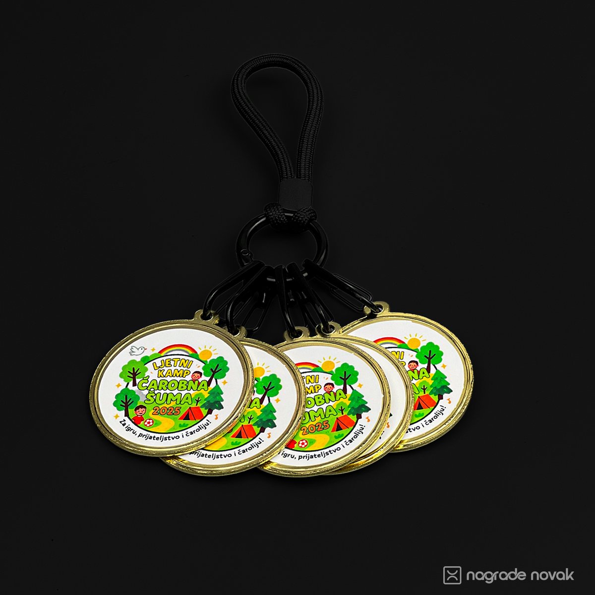 Five small round medals with the camp insert on a black carabiner keyring with a black cord loop, on a dark background