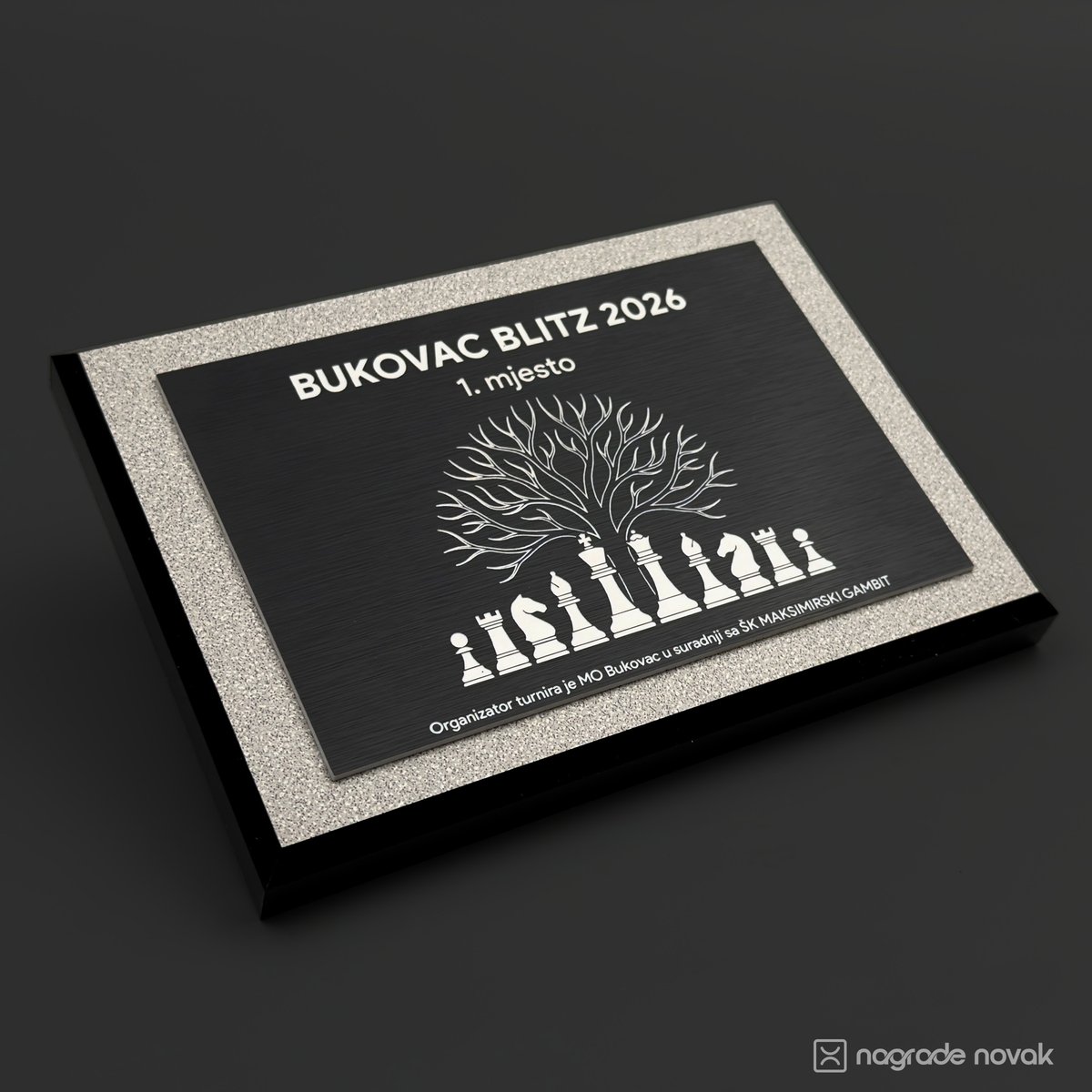 Award plaque engraved "BUKOVAC BLITZ 2026, 1. mjesto" with a tree above chess pieces, seen at an angle on a dark surface