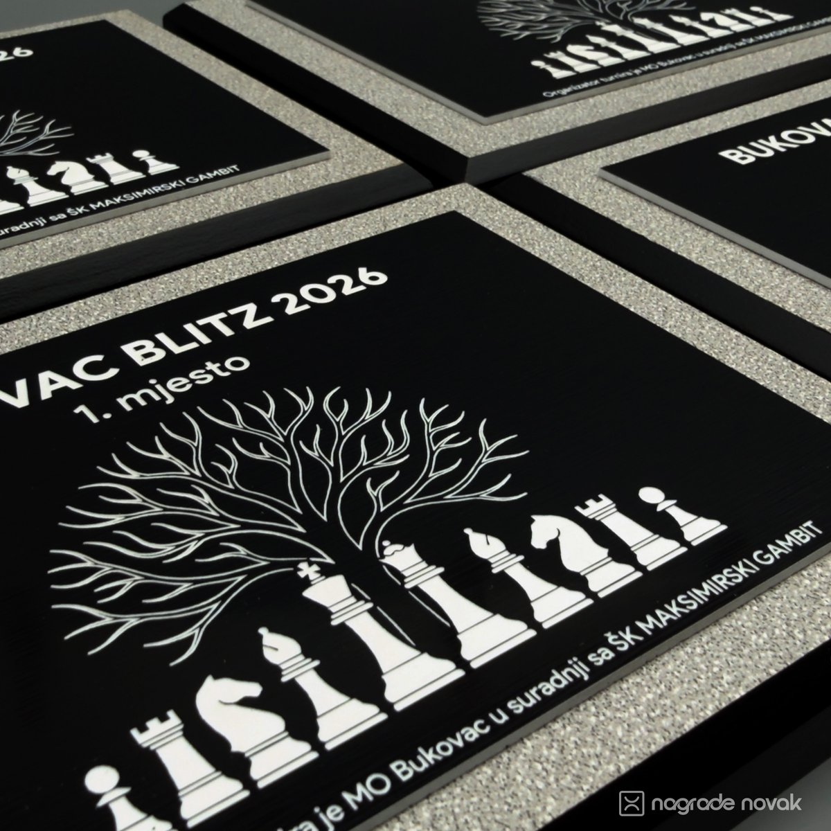 Close-up of several black engraved plaques in grey frames, with the 1st place plaque in front showing a tree above white chess pieces