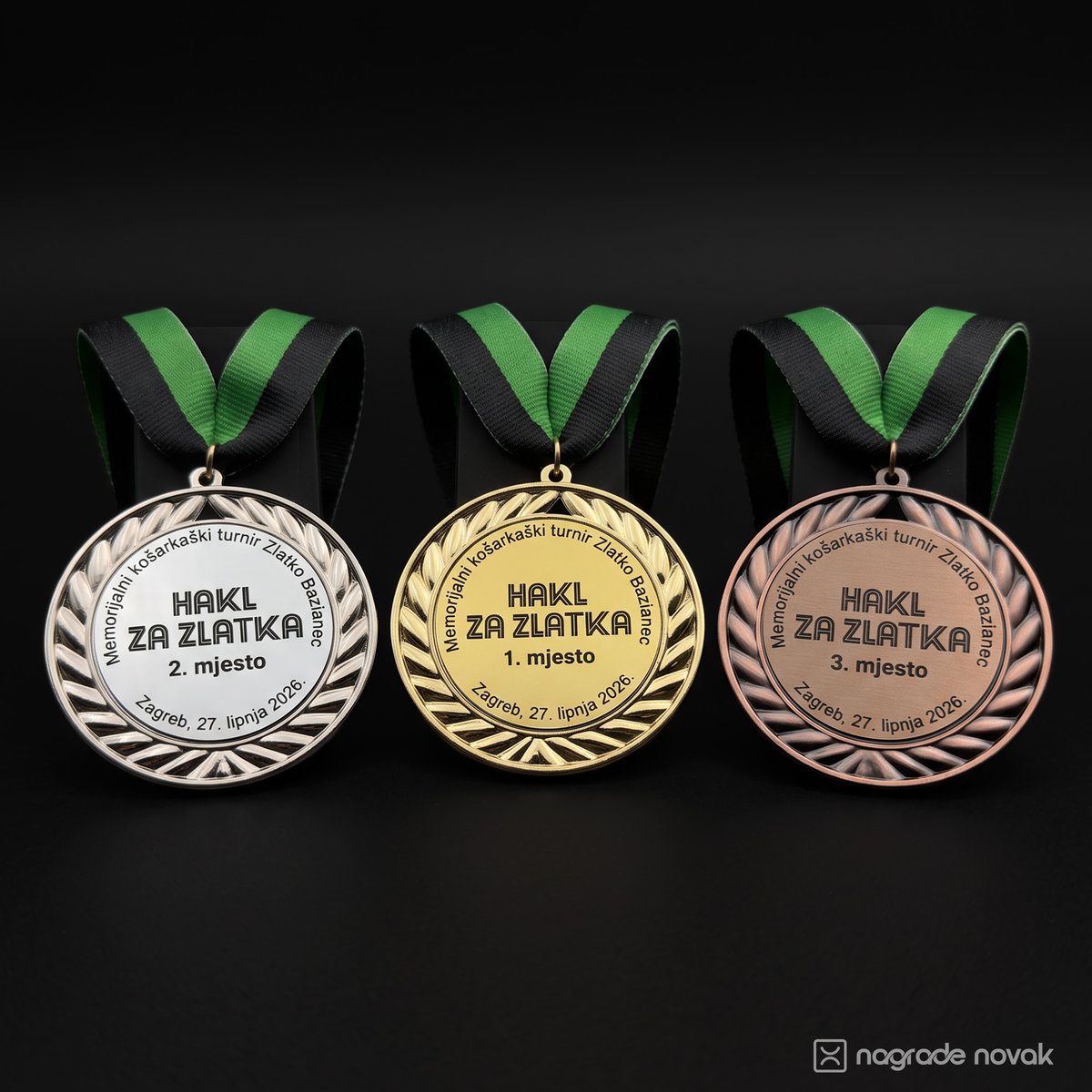Silver, gold and bronze medals hanging side by side on green and black ribbons against a dark background