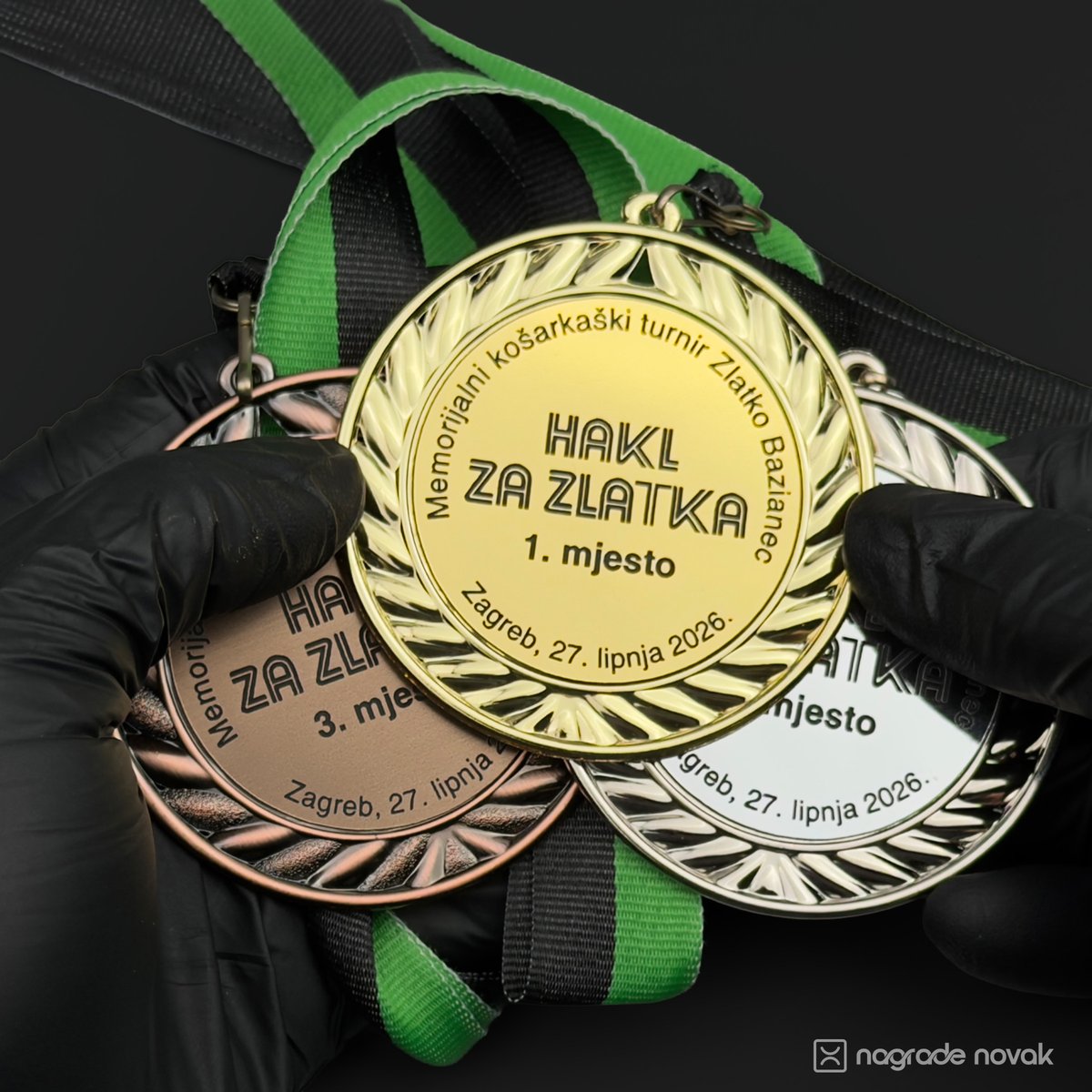 First-person view of black-gloved hands holding the gold 1st place medal in front of the silver and bronze medals on green and black ribbons