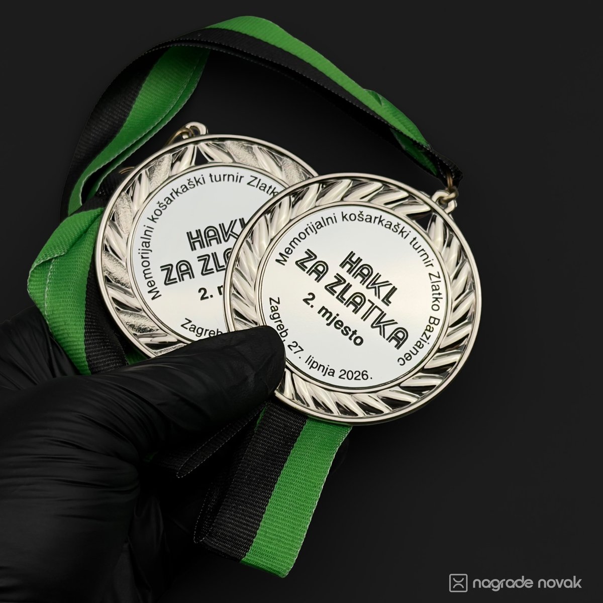First-person view of black-gloved hands holding two silver 2nd place medals on green and black ribbons