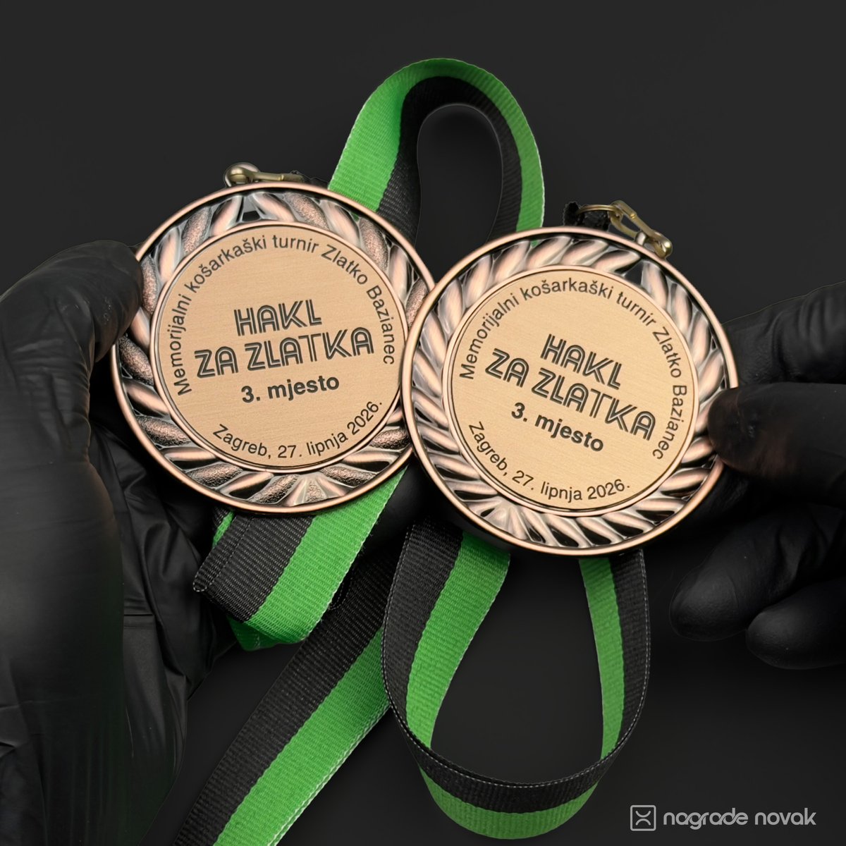 First-person view of black-gloved hands holding two bronze 3rd place medals on green and black ribbons