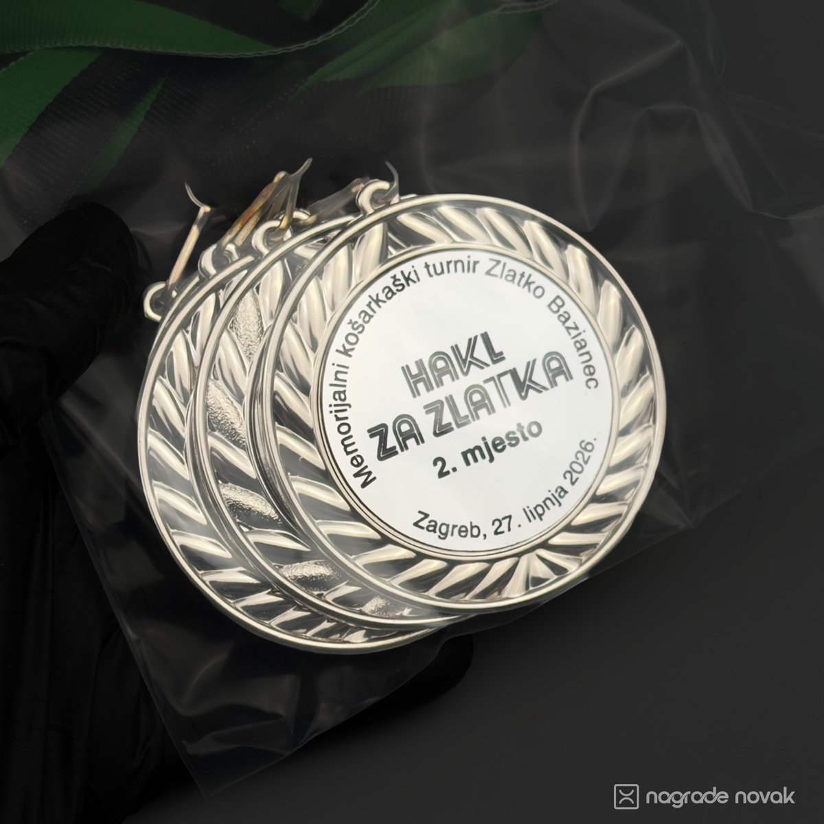 First-person view of a gloved hand holding several silver 2nd place medals packed together in a clear plastic bag